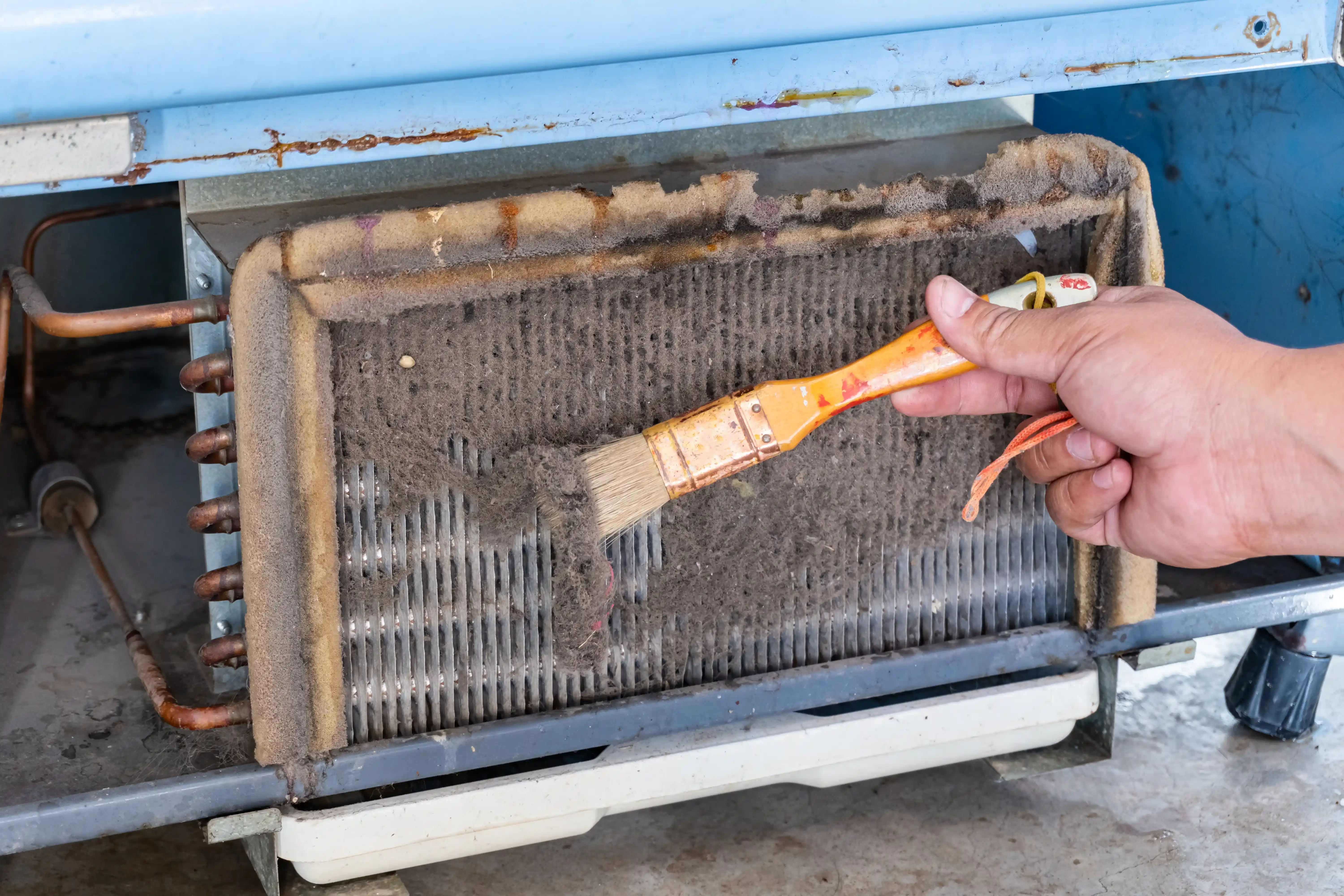 A Professional Heating and Cooling technician cleaning a heavily clogged evaporator coil as part of an AC maintenance service in Nashville, TN.